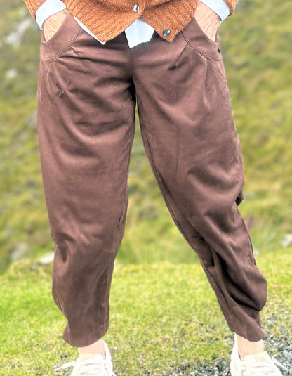 A person wearing brown corduroy pants with a brown cardigan and white sneakers, standing outdoors on a grassy hillside.