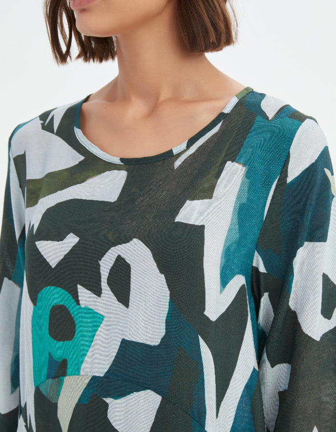Woman wearing a patterned top with abstract design in green, white, and black.