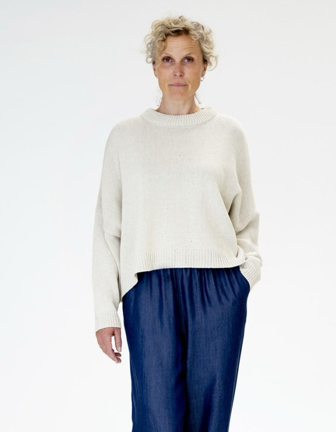 Woman wearing a white sweater and blue pants on a white background