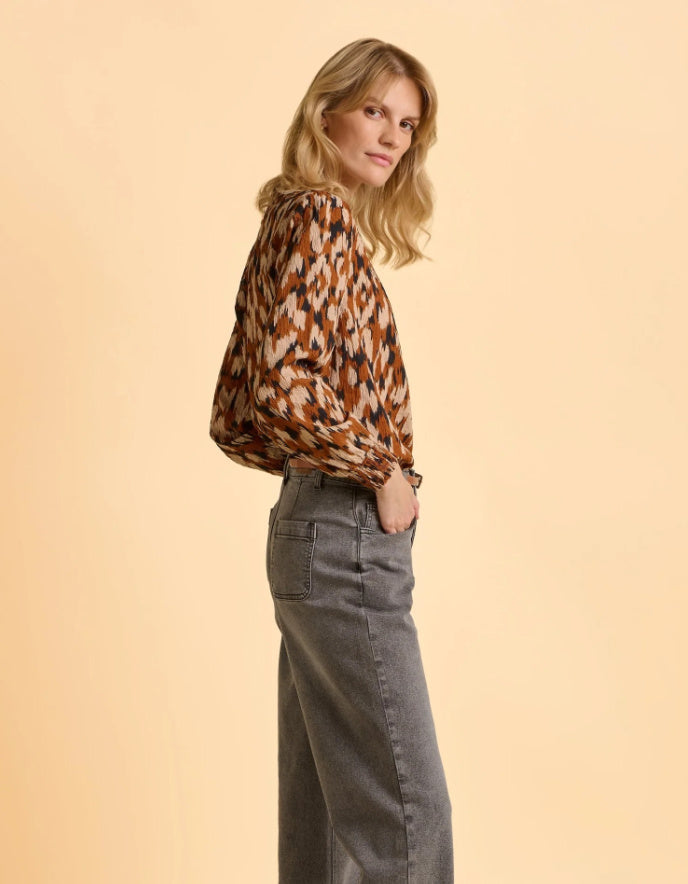 Woman wearing a patterned blouse and jeans on a beige background