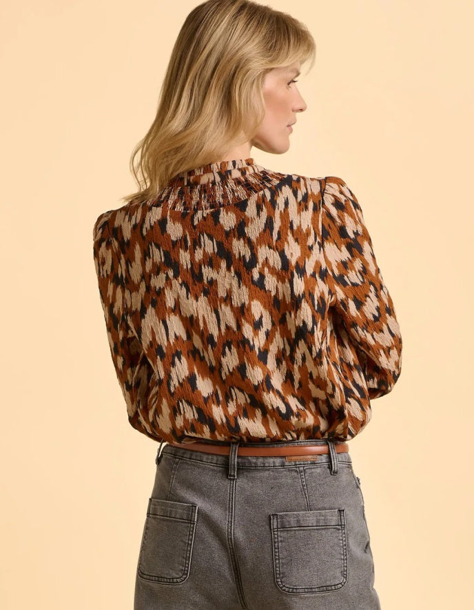 Woman wearing a patterned blouse and gray pants on a beige background