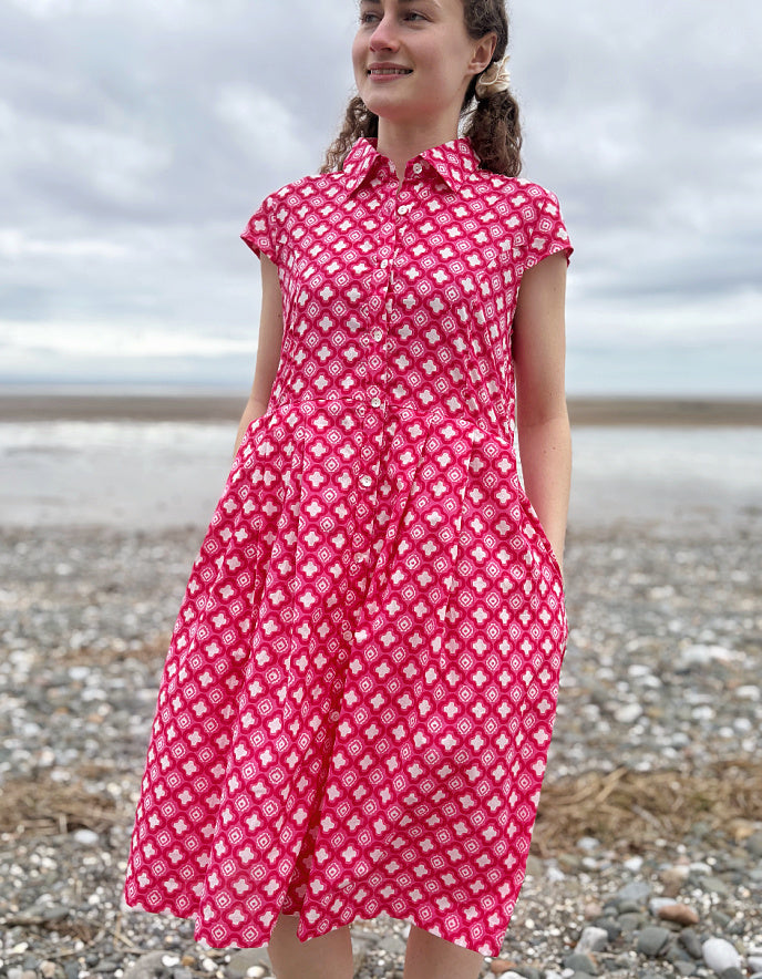 Woman wearing a pink cotton shirt dress with a geometric pattern on a pebbly beach.
