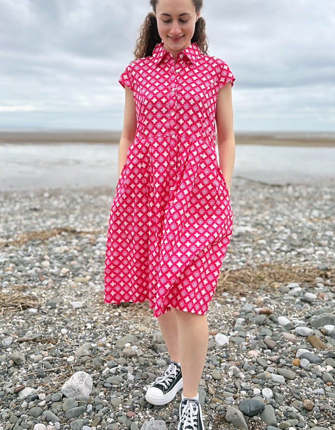 Woman wearing a pink cotton shirt dress with a geometric pattern on a pebbly beach.