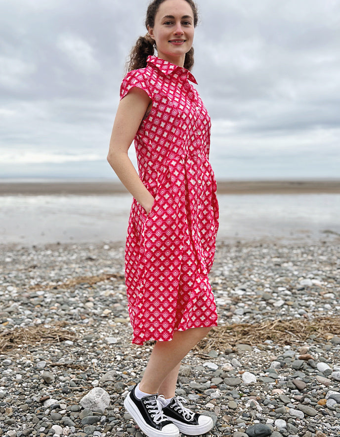 Woman wearing a pink cotton shirt dress with a geometric pattern on a pebbly beach.