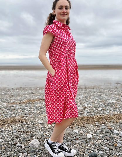 Woman wearing a pink cotton shirt dress with a geometric pattern on a pebbly beach.