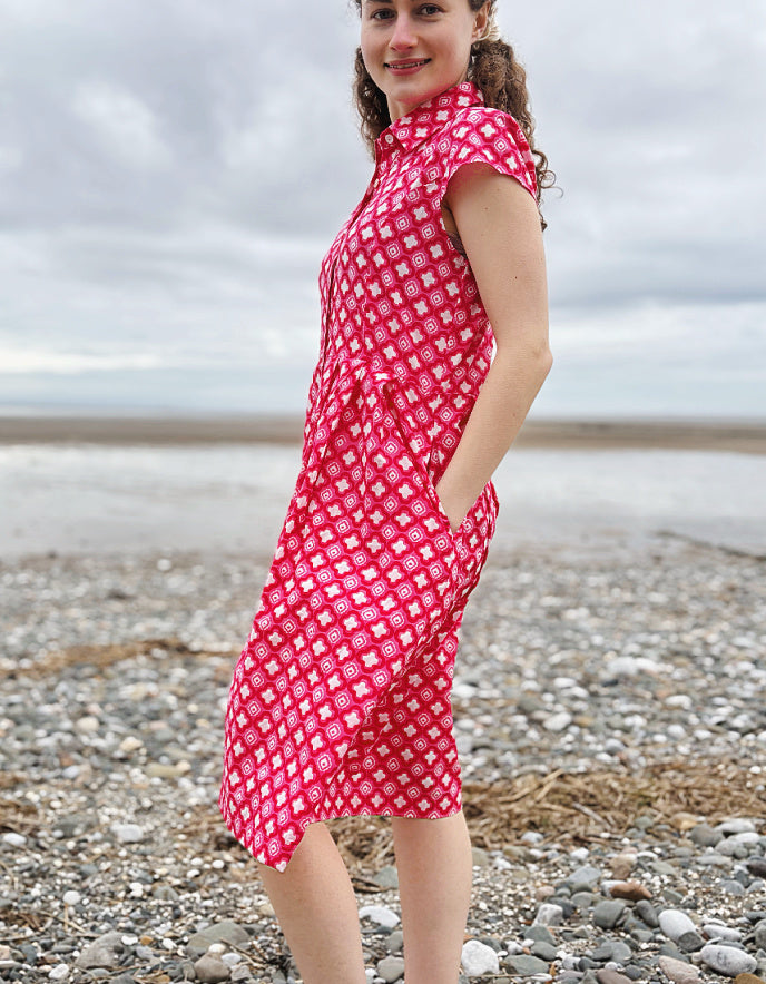 Woman wearing a pink cotton shirt dress with a geometric pattern on a pebbly beach.