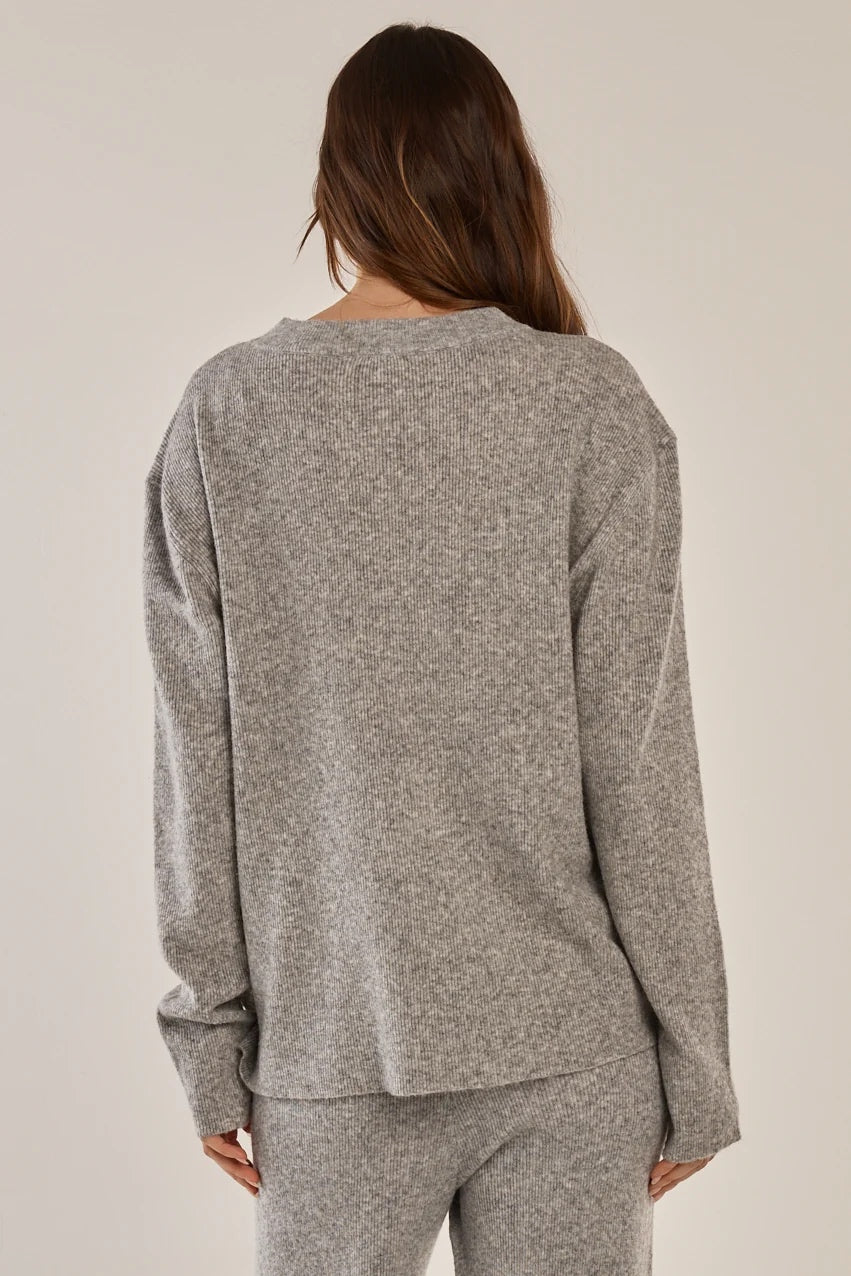 A woman viewed from behind wearing a heather gray long-sleeve knit top and matching gray pants against a plain light beige studio background.