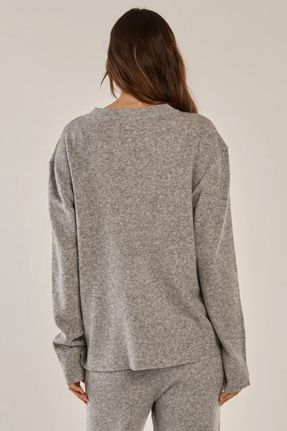 A woman viewed from behind wearing a heather gray long-sleeve knit top and matching gray pants against a plain light beige studio background.