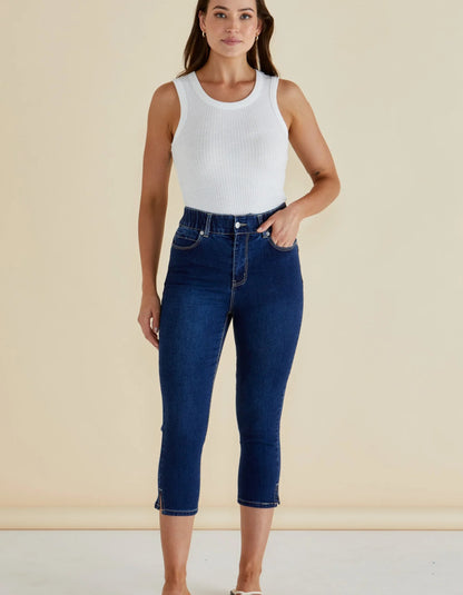 Woman wearing a white tank top and blue jeans against a beige background