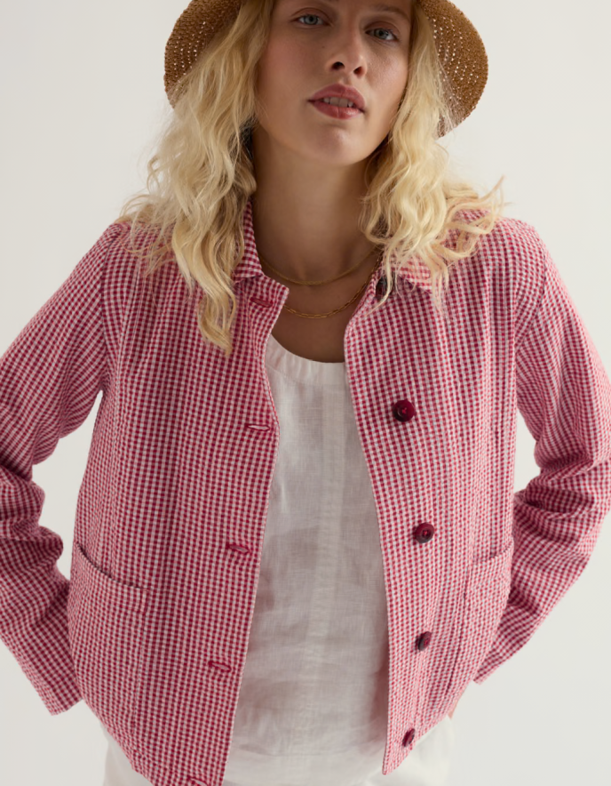Woman wearing a red and white checkered jacket with a straw hat on a plain background