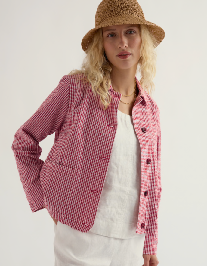 Woman wearing a red and white checkered jacket with a straw hat on a plain background