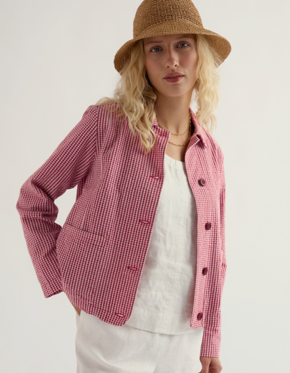 Woman wearing a red and white checkered jacket with a straw hat on a plain background