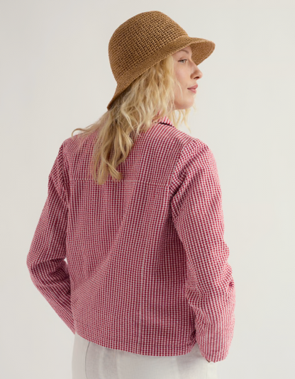 Woman wearing a red and white checkered jacket with a straw hat on a plain background