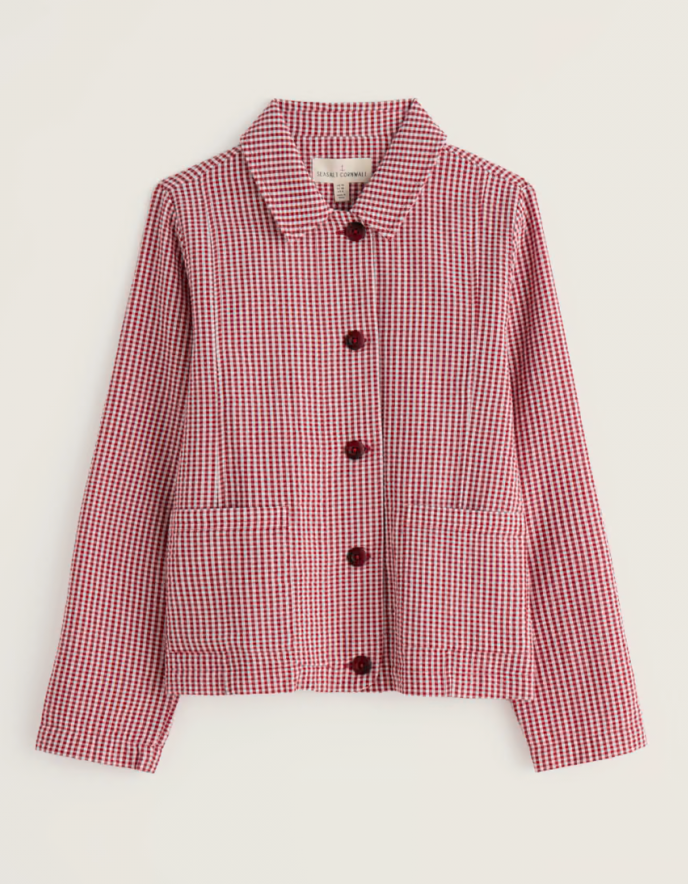 Woman wearing a red and white checkered jacket with a straw hat on a plain background