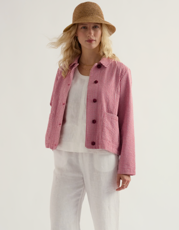 Woman wearing a red and white checkered jacket with a straw hat on a plain background