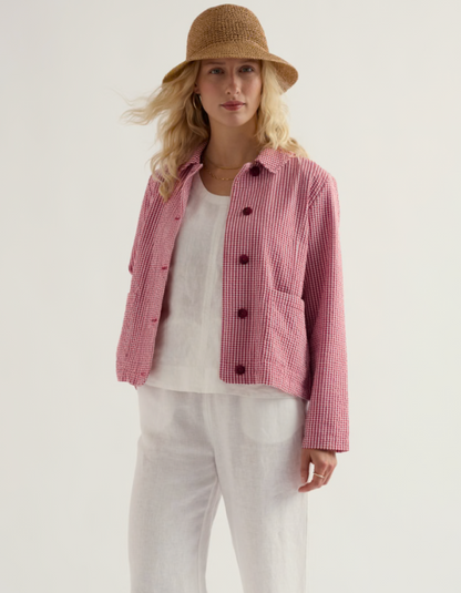 Woman wearing a red and white checkered jacket with a straw hat on a plain background