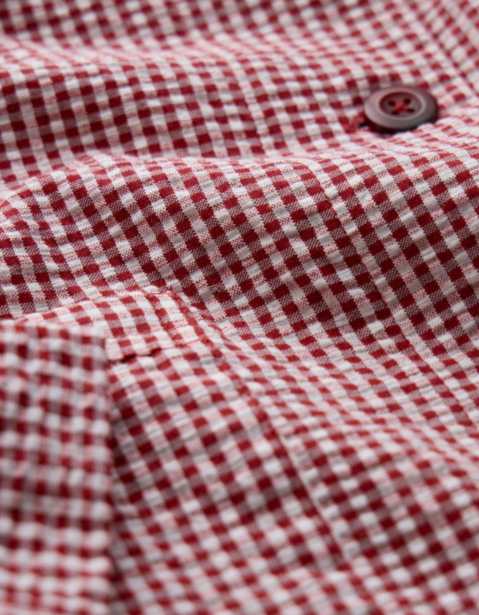 Woman wearing a red and white checkered jacket with a straw hat on a plain background