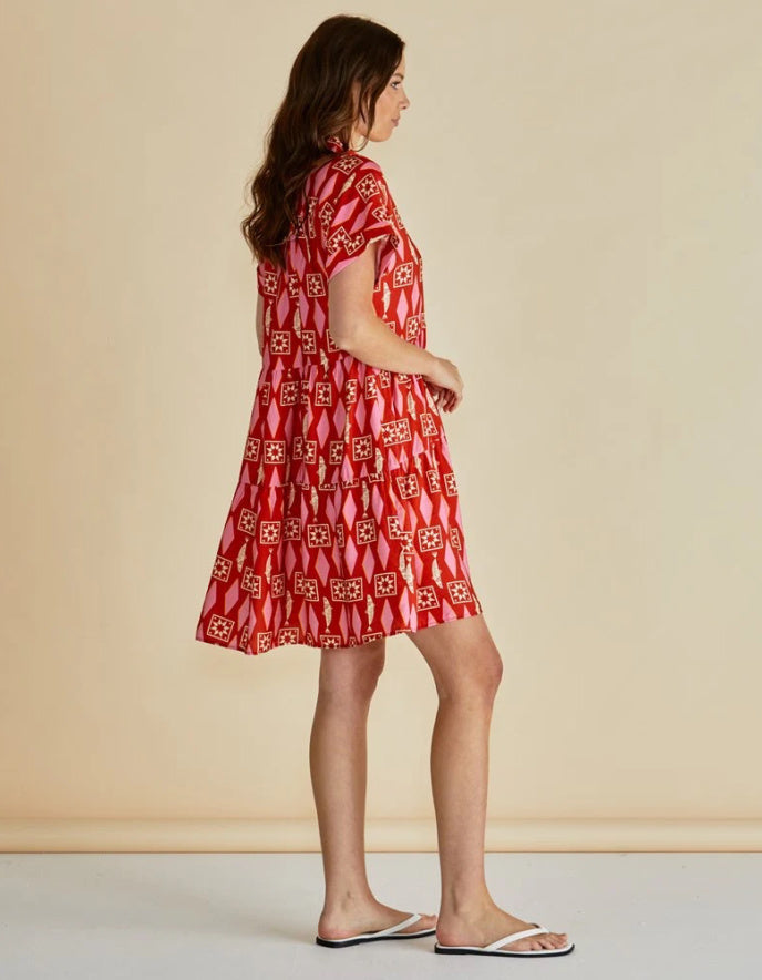 Woman wearing a red and pink  patterned shirt dress against a beige background