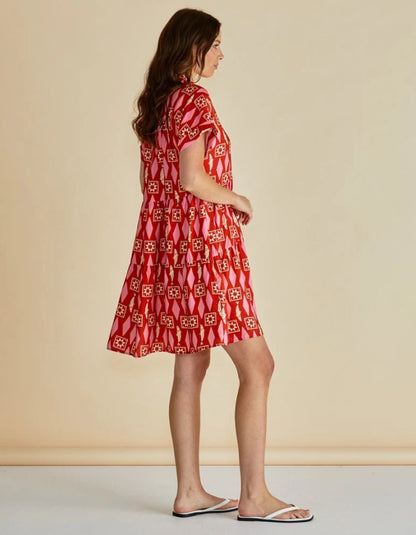 Woman wearing a red and pink  patterned shirt dress against a beige background
