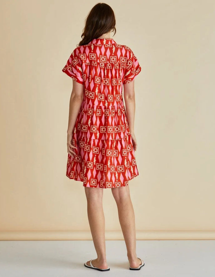 Woman wearing a red and pink  patterned shirt dress against a beige background