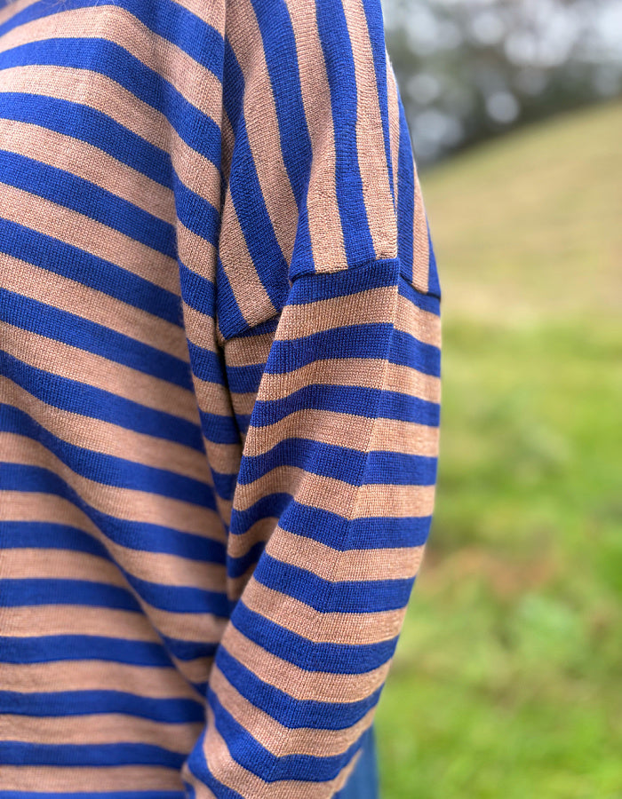A close-up of a person wearing a blue and tan striped knit top, photographed outdoors with a blurred green grassy background.