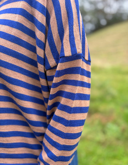 A close-up of a person wearing a blue and tan striped knit top, photographed outdoors with a blurred green grassy background.