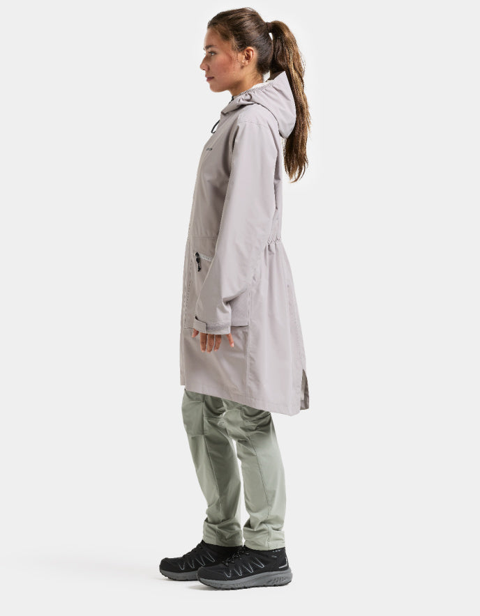 Person wearing a light gray trench coat and pants on a white background