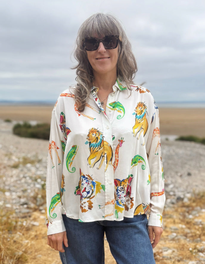 A woman wearing a long-sleeve button-up shirt with a colorful cartoon animal print, standing outdoors in a rocky, grassy landscape under an overcast sky.