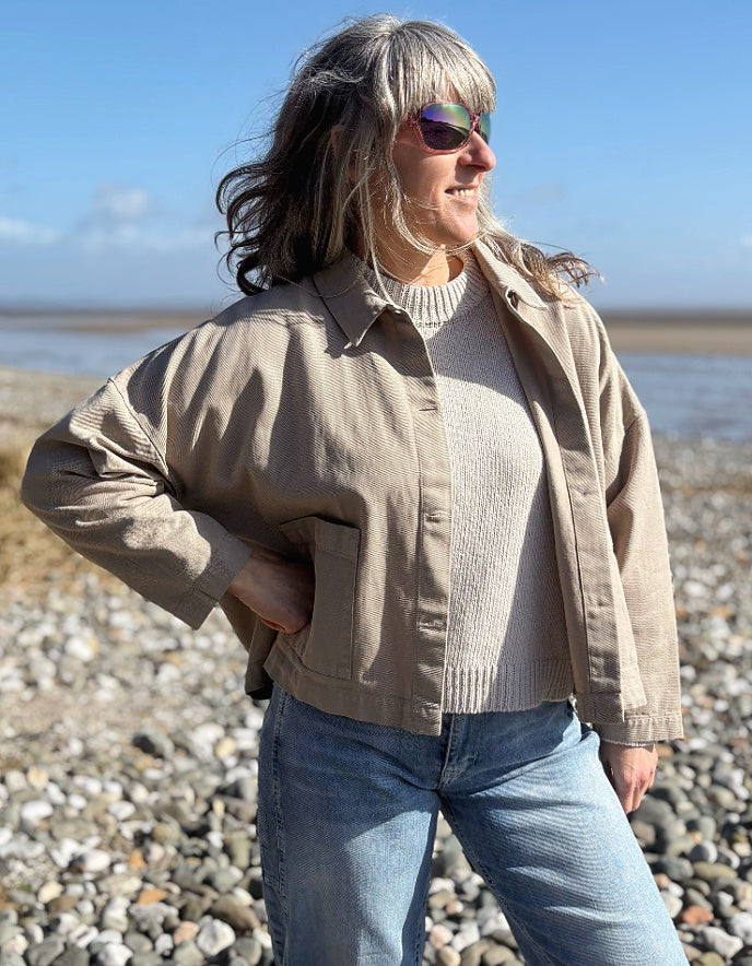 woman wearing sandy cotton workwear inspired jacket and jeans on a beach