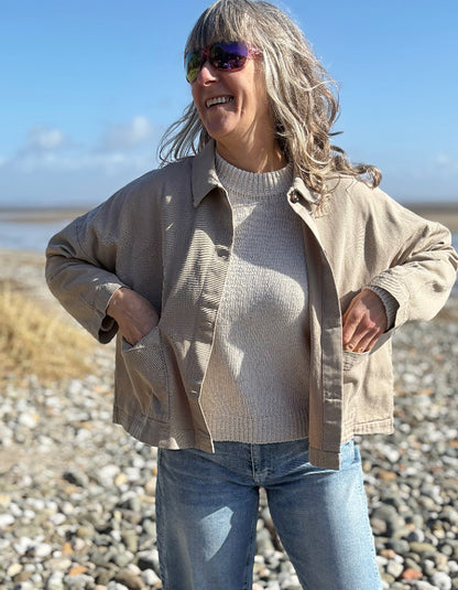 woman wearing sandy cotton workwear inspired jacket and jeans on a beach