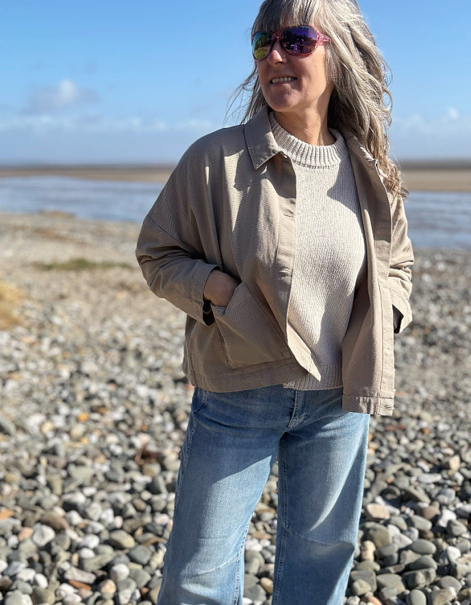 woman wearing sandy cotton workwear inspired jacket and jeans on a beach