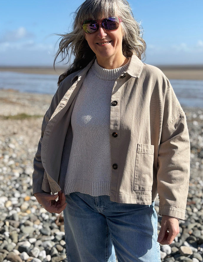 woman wearing sandy cotton workwear inspired jacket and jeans on a beach
