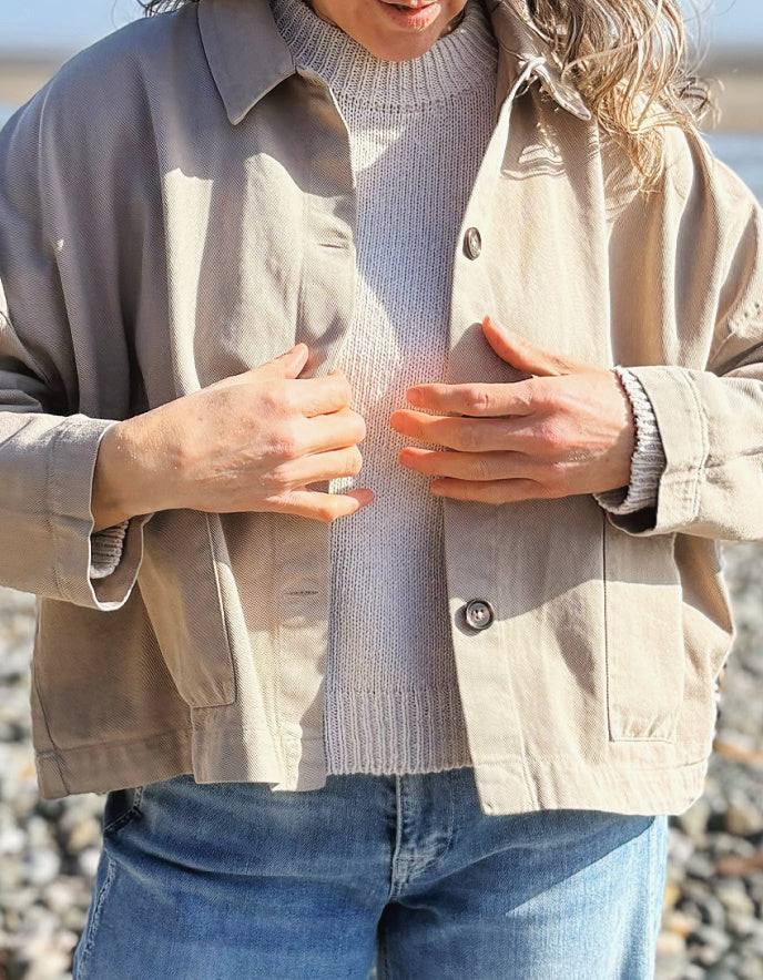 woman wearing sandy cotton workwear inspired jacket and jeans on a beach
