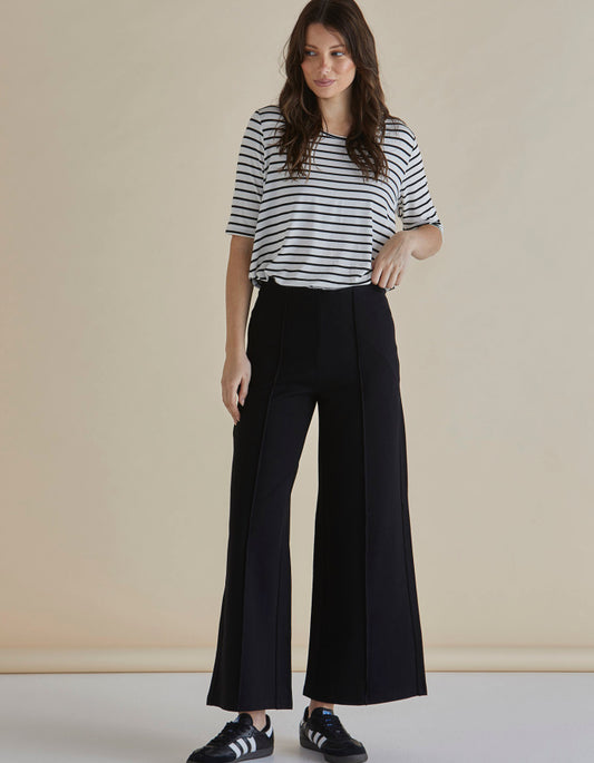 Woman wearing a striped shirt and black wide-leg pants on a beige background