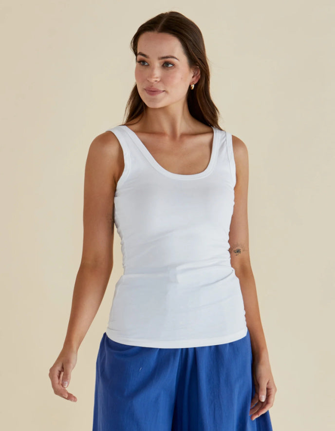 Woman wearing a white tank top and blue pants against a beige background