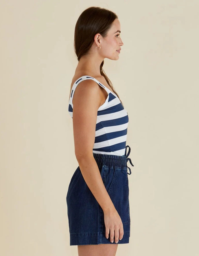 Woman wearing a navy and white striped tank top and dark denim skirt on a beige background