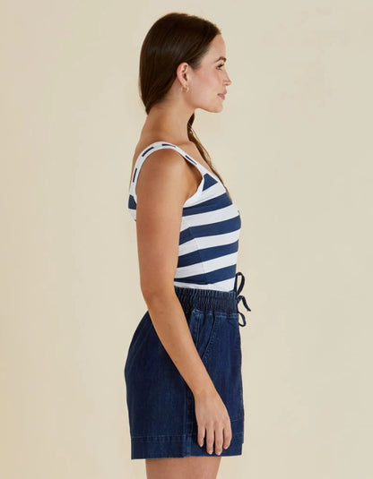 Woman wearing a navy and white striped tank top and dark denim skirt on a beige background
