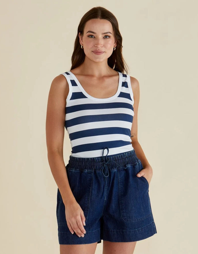 Woman wearing a navy and white striped tank top and blue shorts on a beige background