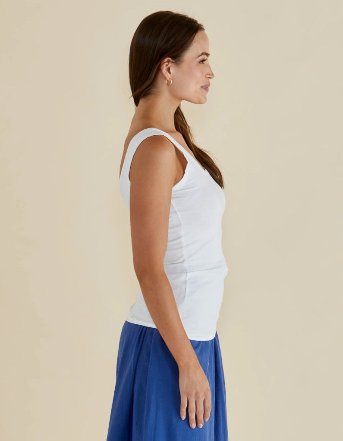 Woman wearing a white tank top and blue skirt on a beige background