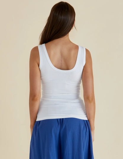 Woman wearing a white tank top and blue pants on a beige background