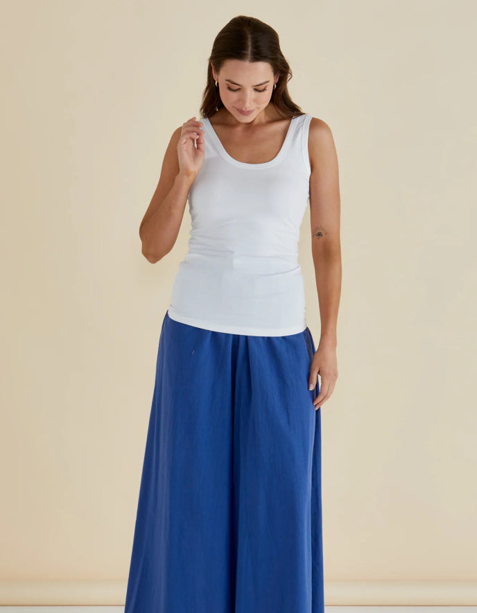 Woman wearing a white tank top and blue pants on a beige background