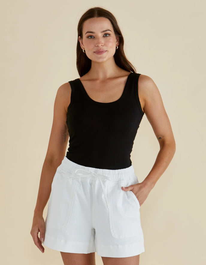 Woman wearing a black tank top and white shorts on a beige background
