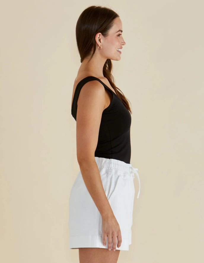 Woman wearing a black top and white skirt against a beige background