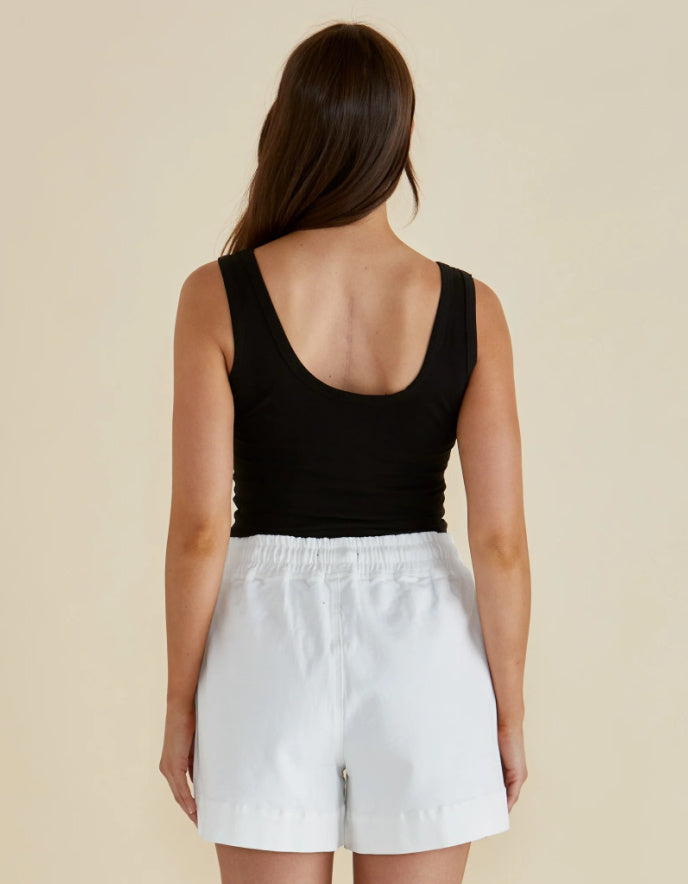 Person wearing a black tank top and white shorts on a beige background