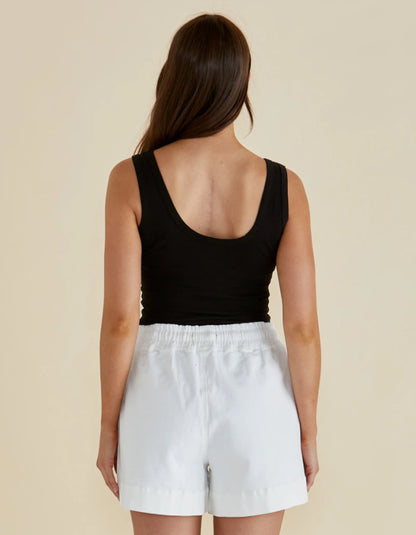 Person wearing a black tank top and white shorts on a beige background