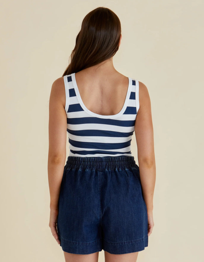Woman wearing a navy and white striped tank top and dark blue shorts on a beige background
