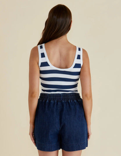 Woman wearing a navy and white striped tank top and dark blue shorts on a beige background