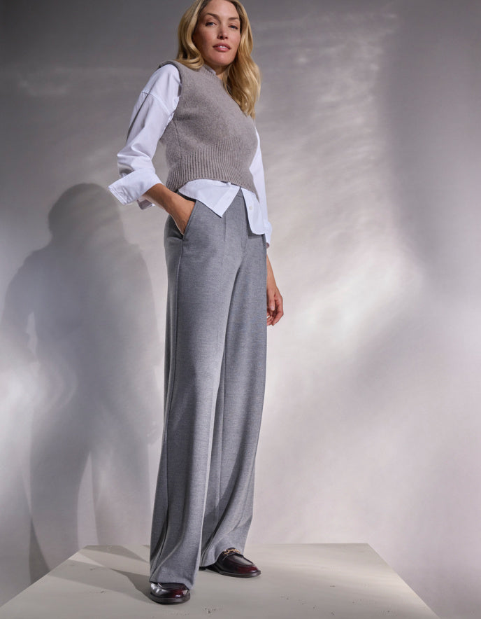 Woman wearing a gray sweater vest over a white blouse and gray wide-leg pants against a neutral background