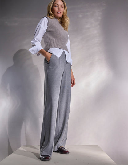 Woman wearing a gray sweater vest over a white blouse and gray wide-leg pants against a neutral background