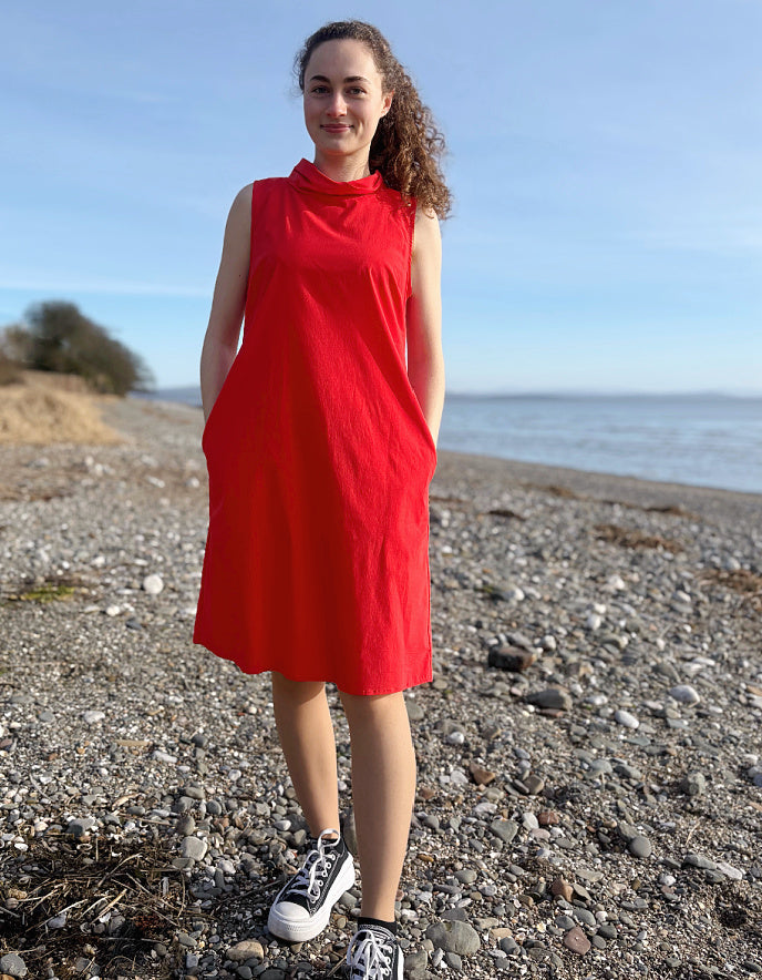 Person wearing a red dress standing on a pebbly beach with ocean and sky in the background